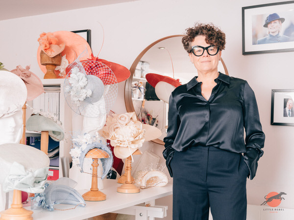 Milliner Justine Bradley-Hill standing among handcrafted hats and fascinators in her studio
