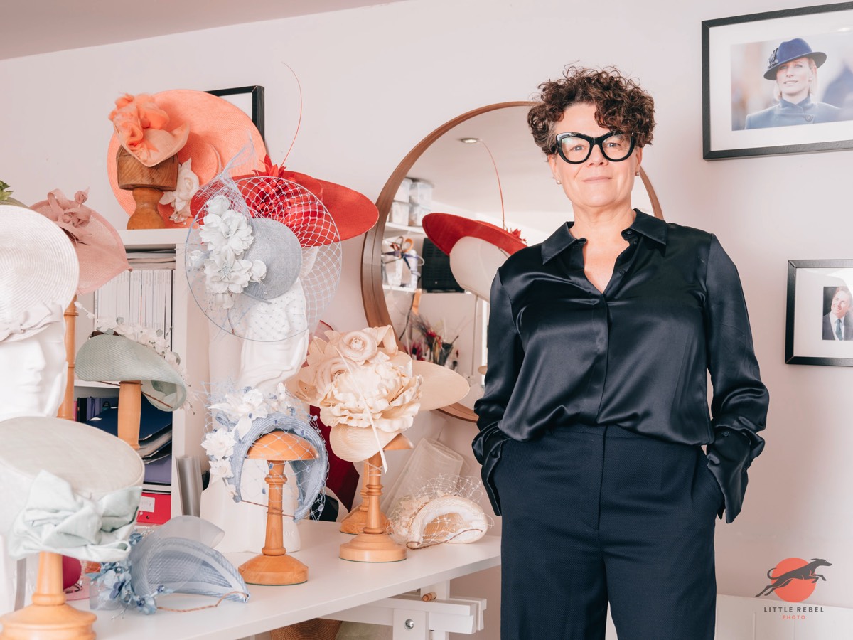Milliner Justine Bradley-Hill standing among handcrafted hats and fascinators in her studio
