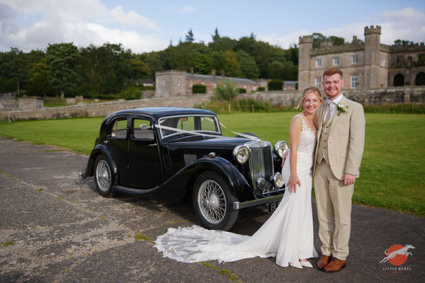 Newlyweds beside a vintage MG VA wedding car outside Lowther Castle in Cumbria