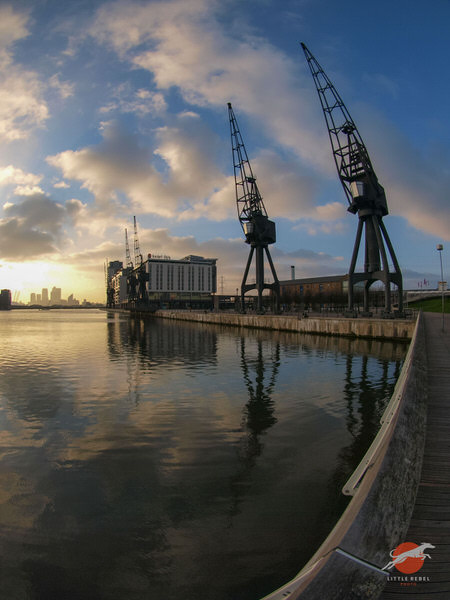 Historic dock cranes reflected in Royal Victoria Dock at sunset in East London
