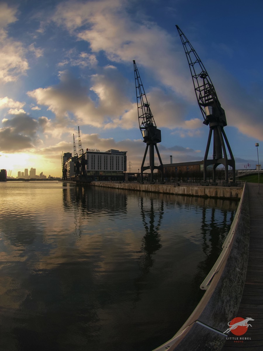 Historic dock cranes reflected in Royal Victoria Dock at sunset in East London