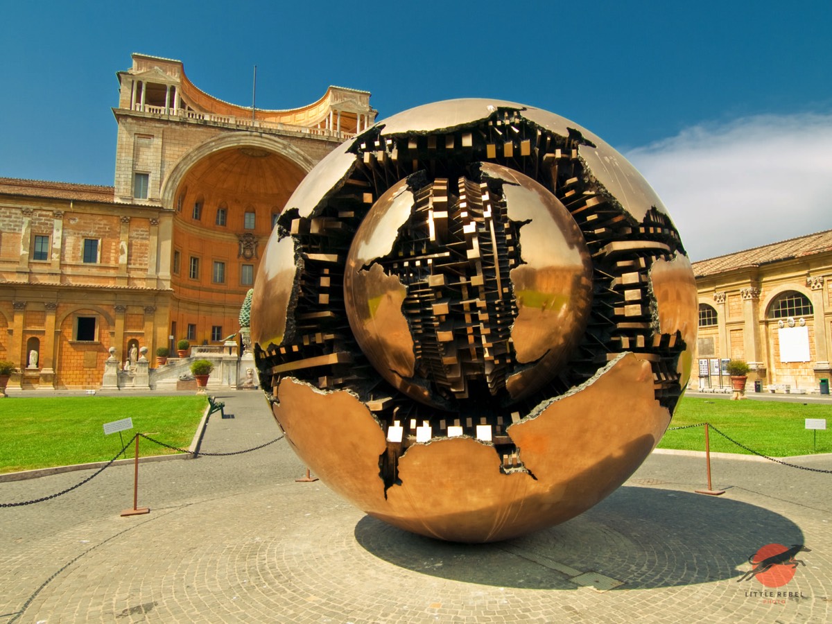 This bronze sculpture is named Sfera con Sfera (Sphere Within Sphere) and was created by Italian sculptor Arnaldo Pomodoro