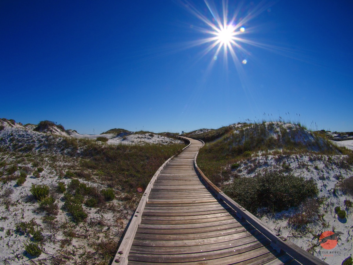 Wooden boardwalk winding through white sand dunes at WaterSound Beach in Florida